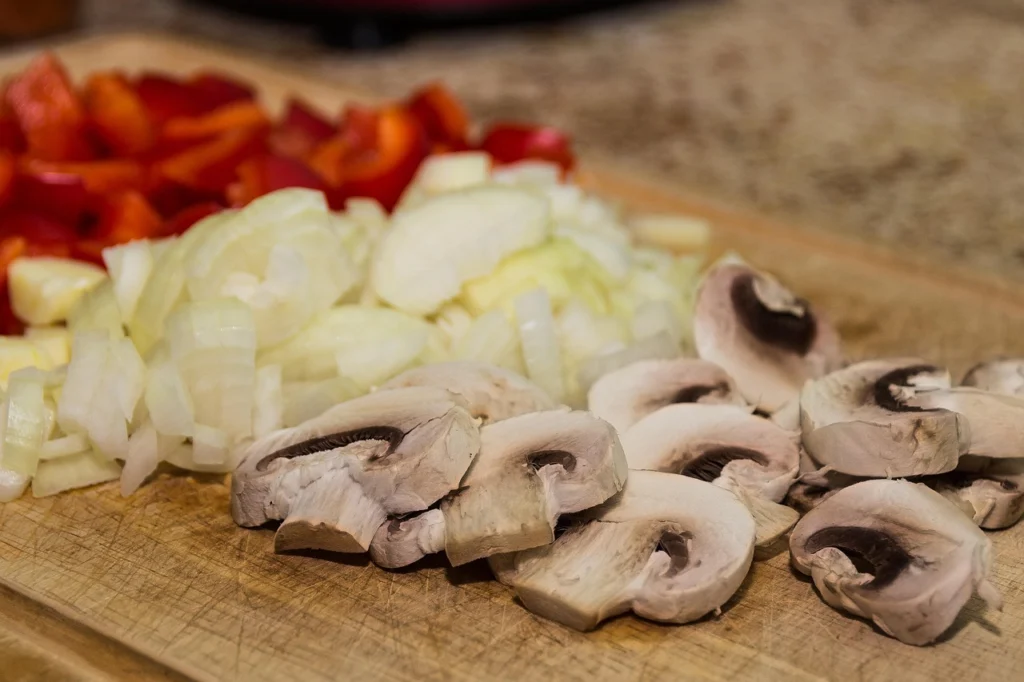 Hands chopping bell peppers and onions on a cutting board for meal prep healthy lunches
